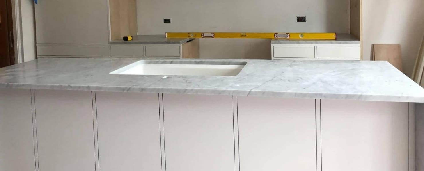 Elegant Carrara marble waterfall island and integrated sink installation by MG Contractor NY, highlighting precision veining and high-end natural stone craftsmanship