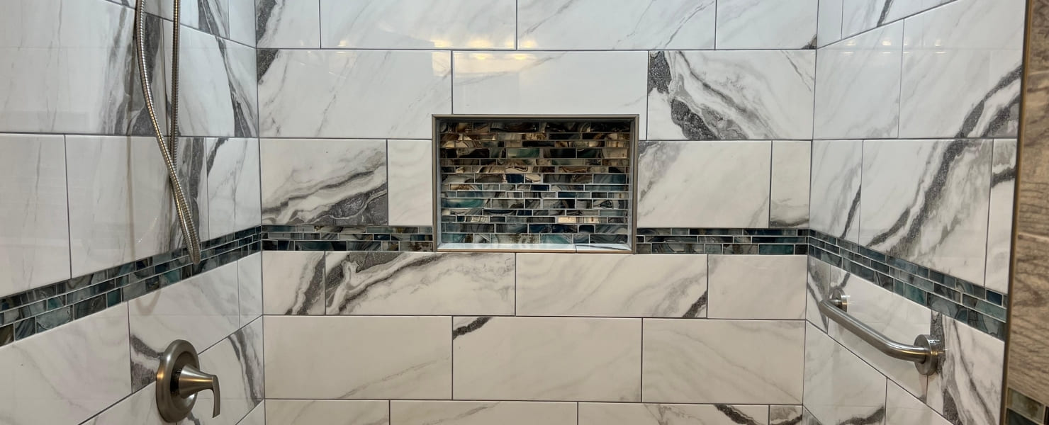 Finished view of a clean, minimalist walk-in shower stall featuring large white marble subway tiles on the walls and complementary gray wood-look plank tiles on the accent pillar and floor