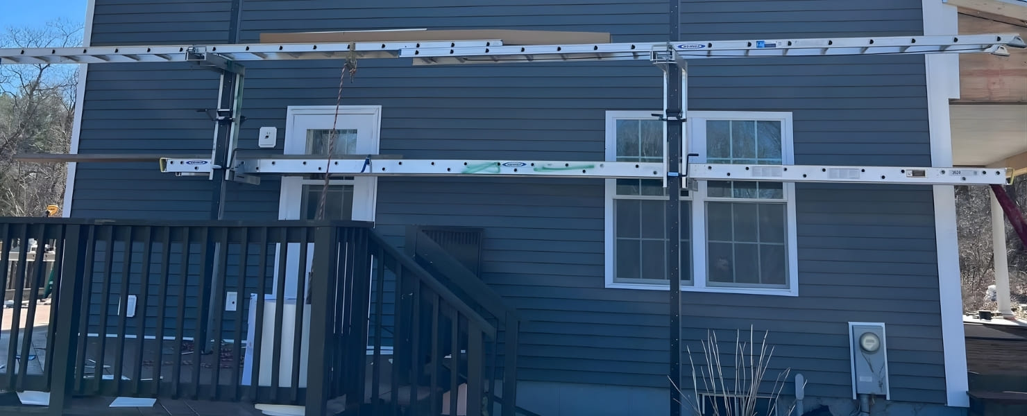 Professional installation of dark gray vinyl siding and white aluminum soffit on a two-story home in Albany, NY, by MG Contractor NY, using pump jack scaffolding for a seamless finish